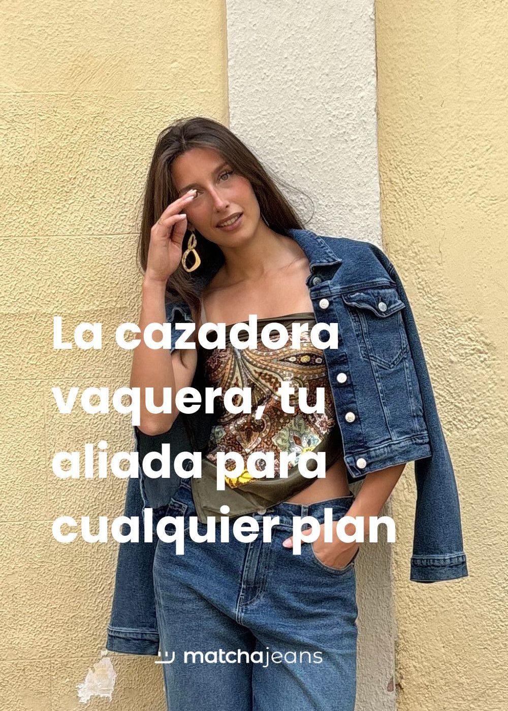 Chica morena con cazadora vaquera azul oscuro, top de estampado verde brillante y pantalones vaqueros azules.