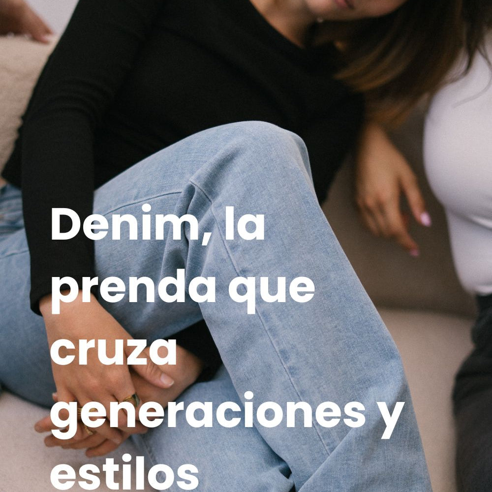 Chica con pelo corto pelirrojo está sentada en un sofá con las piernas cruzadas, lleva una camiseta de manga larga negra y vaqueros azules