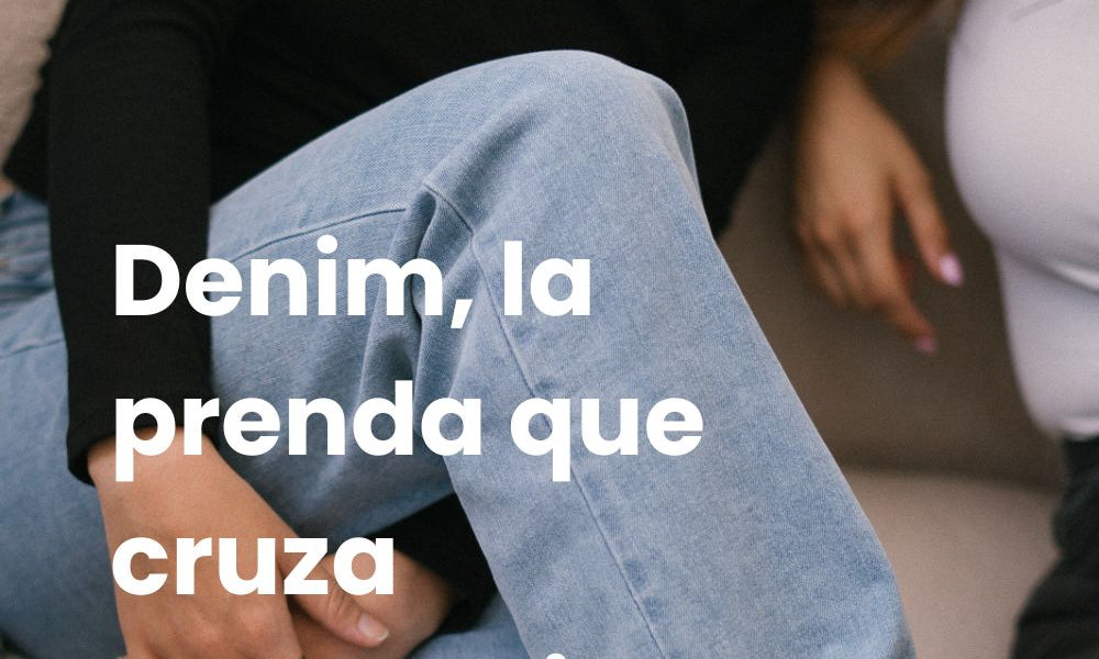 Chica con pelo corto pelirrojo está sentada en un sofá con las piernas cruzadas, lleva una camiseta de manga larga negra y vaqueros azules